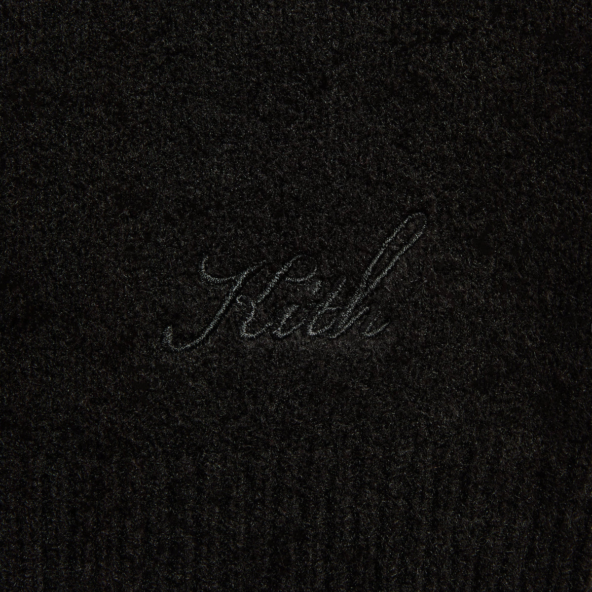 Close-up of the tonal 'Kith' script on the black Harmon henley sweater