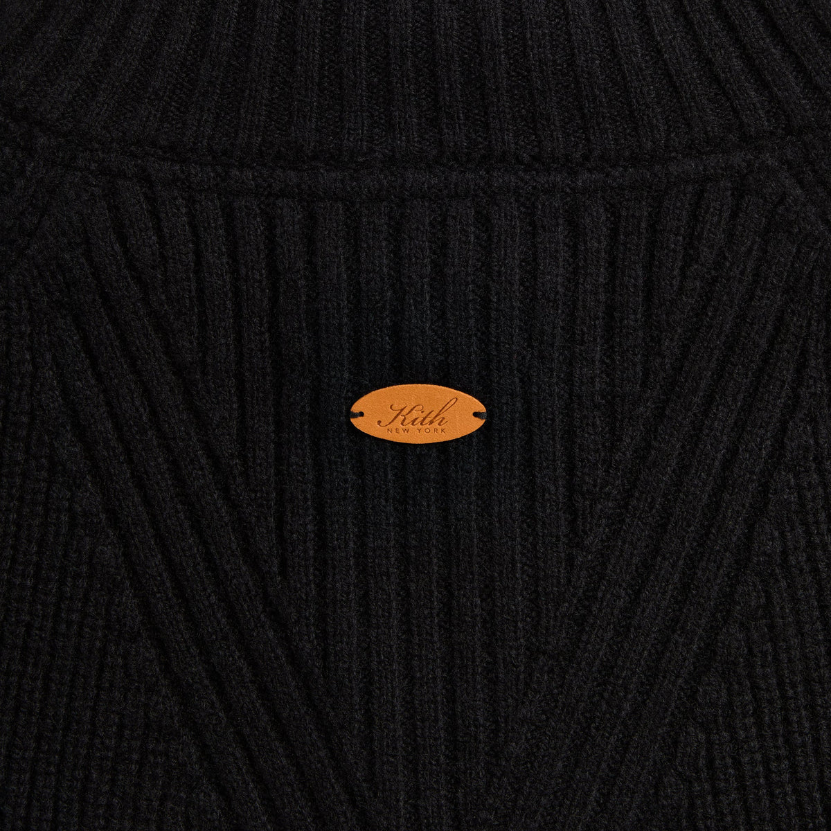 Close-up of the tan oval Kith leather label on the black Marled Copeland quarter-zip