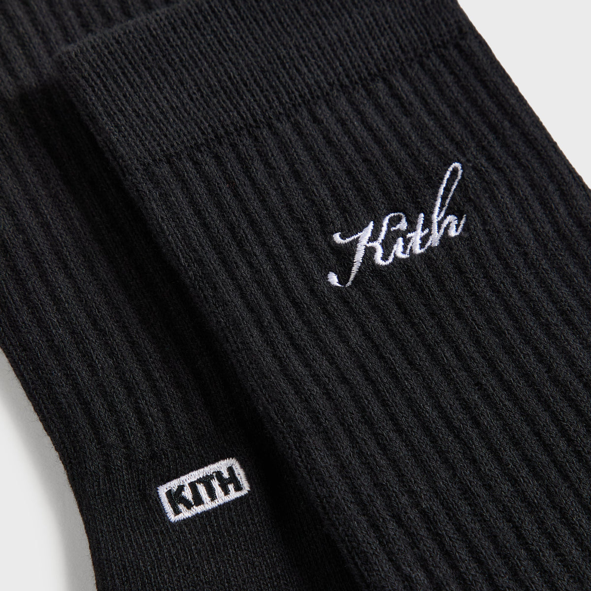 Close-up of the white 'Kith' script and KITH box logo on the black ribbed crew socks